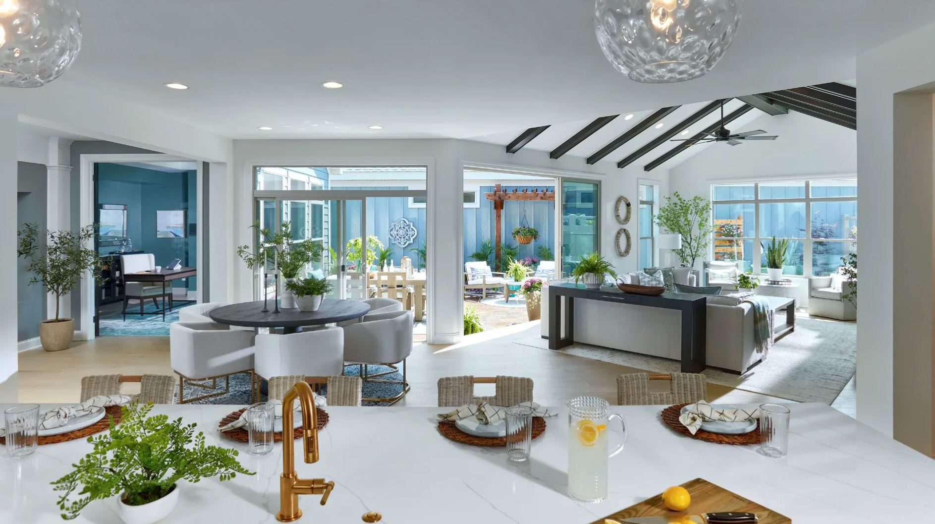 chipeta-hollows-home-interior Modern open-concept kitchen, dining, and living space in a Chipeta Hollows home, featuring bright natural light, vaulted ceilings with exposed beams, indoor-outdoor patio access, and stylish low-maintenance finishes.